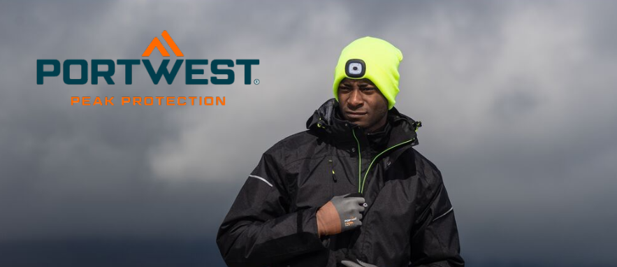 Immagine di un operaio in abiti da lavoro neri. L'uomo indossa guanti e un berretto giallo con luce LED integrata. Sullo sfondo sono visibili nuvole scure e un paesaggio nebbioso.