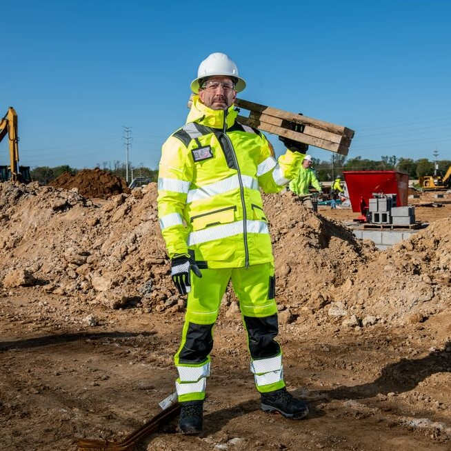 Uomo in abbigliamento da lavoro giallo ad alta visibilità in un cantiere sotto un cielo blu.