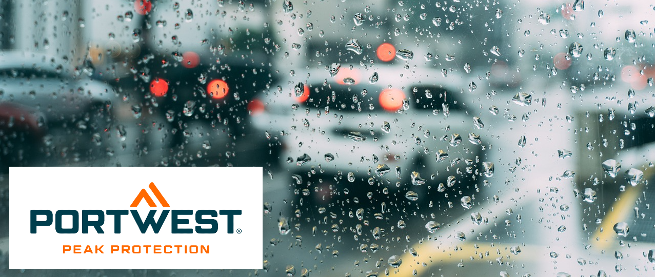 Strada bagnata di pioggia con auto fotografate attraverso una finestra coperta di gocce di pioggia. Nell'angolo in basso a sinistra c'è il logo Portwest blu e arancione su sfondo bianco.
