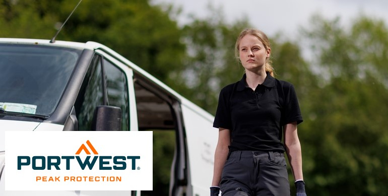 Una donna che indossa una polo nera e pantaloni da lavoro grigi sta davanti a un furgone bianco all'aperto. Sullo sfondo si possono vedere alberi verdi. In basso a sinistra dell'immagine c'è il logo di "Portwest Peak Protection"