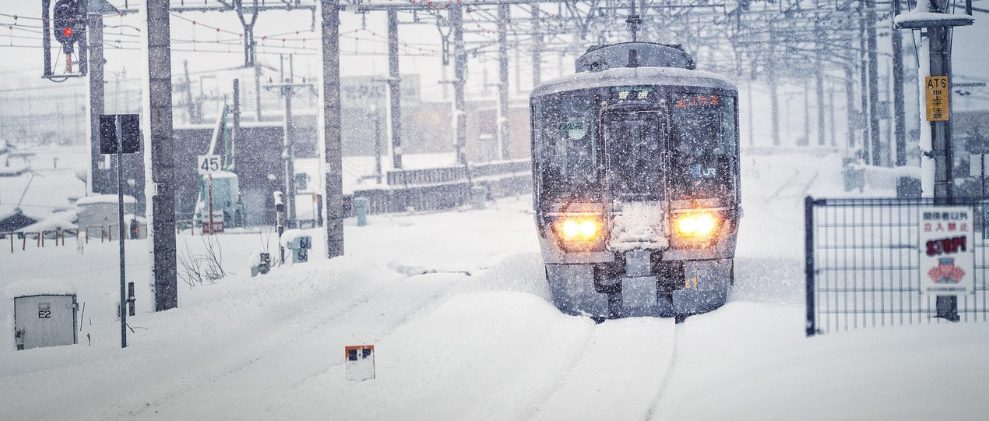 Vista frontale di un treno. I binari sono coperti di neve e la visibilit&agrave; &egrave; scarsa a causa della neve che cade.