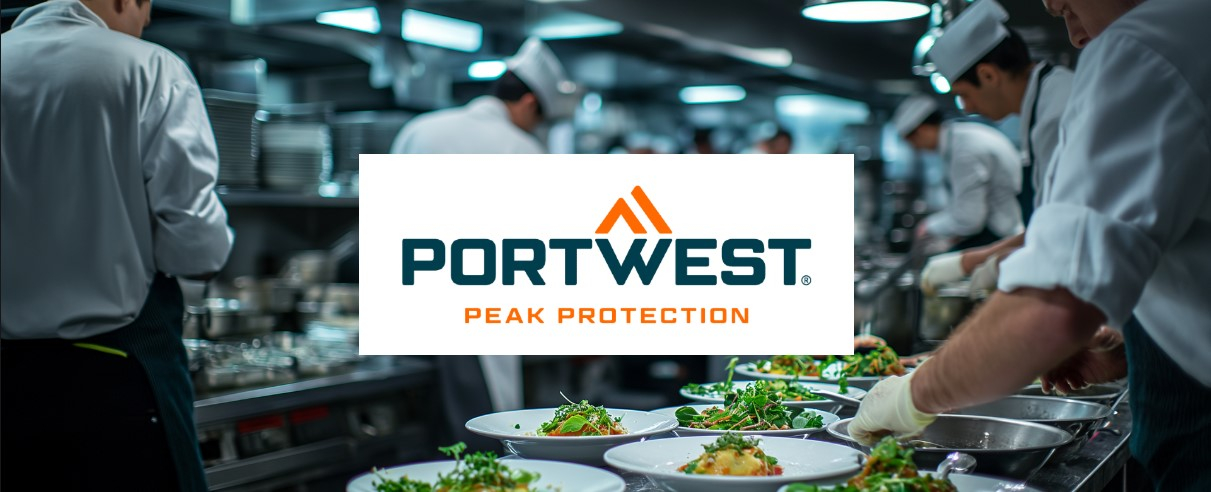 Una cucina commerciale con diversi chef in divisa bianca che lavorano in postazioni diverse e dispongono il cibo sui piatti. L'attenzione è rivolta ai piatti preparati al momento. Il logo Portwest "Peak Protection" è posizionato centralmente sopra l'immagine.