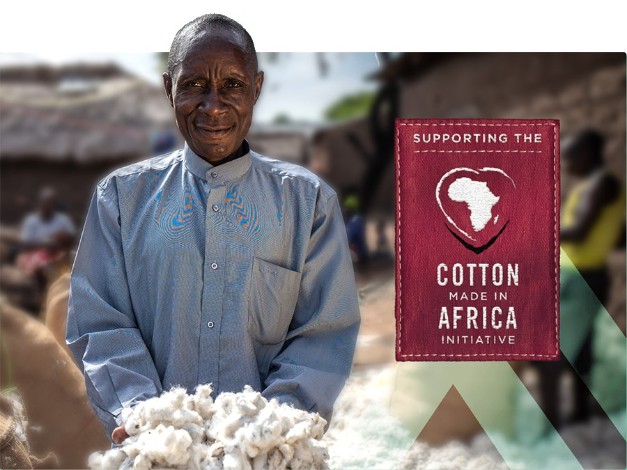 Contadino africano che indossa una camicia blu e presenta una manciata di cotone. Un cartello rosso intenso con la scritta "Supporting the Cotton Made In Africa Initiative" si trova nella metà destra dell'immagine.