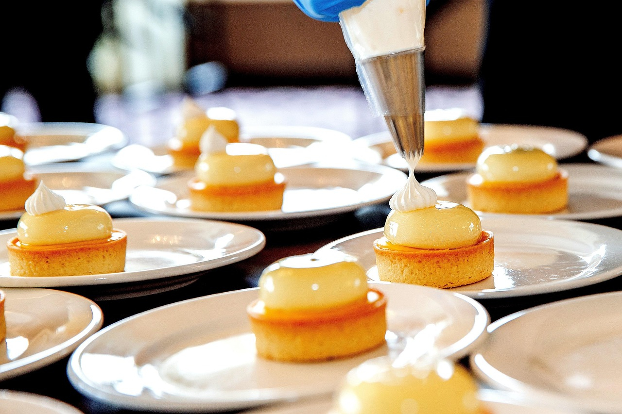 Piatto con pasticceria fine. Una mano con un guanto blu tiene una sac &agrave; poche e spruzza una massa bianca su una tortina.