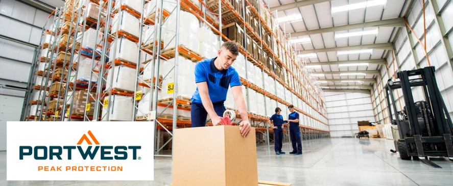 Un magazziniere in abiti da lavoro blu sta sigillando una grande scatola con del nastro adesivo in un moderno e luminoso magazzino a scaffalature alte. Sullo sfondo si vedono altri due dipendenti che chiacchierano. Il logo Portwest con lo slogan "Peak Protection" è visualizzato in basso a sinistra nell'immagine.