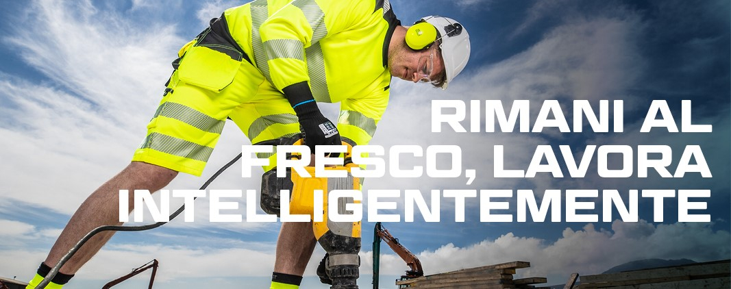 Lavoratore con casco e protezione dell'udito in abiti da lavoro estivi gialli ad alta visibilità che lavora con un martello pneumatico, sullo sfondo blu, cielo leggermente nuvoloso, escavatore e pila di assi di legno.