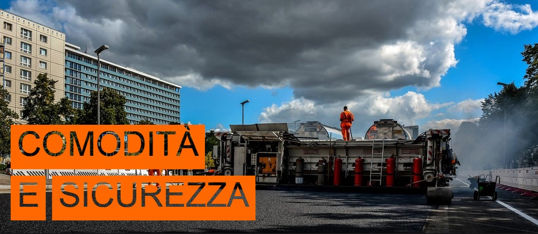 Scena di un cantiere stradale. A sinistra dell'immagine si possono vedere grattacieli e alcuni alberi, la parte destra dell'immagine è coperta da una fontana. Nel bordo inferiore sinistro dell'immagine si trovano le parole “Comfort e Sicurezza” in lettere ritagliate su sfondo arancione.