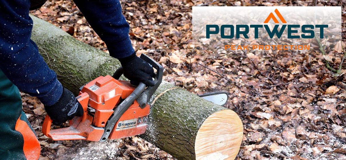 Si vede una persona che usa una motosega per segare un tronco d'albero steso a terra. Sullo sfondo si vedono foglie autunnali marroni e trucioli di legno volanti. Nell'angolo in alto a destra dell'immagine c'è il logo Portwest in blu e arancione su uno sfondo bianco trasparente.